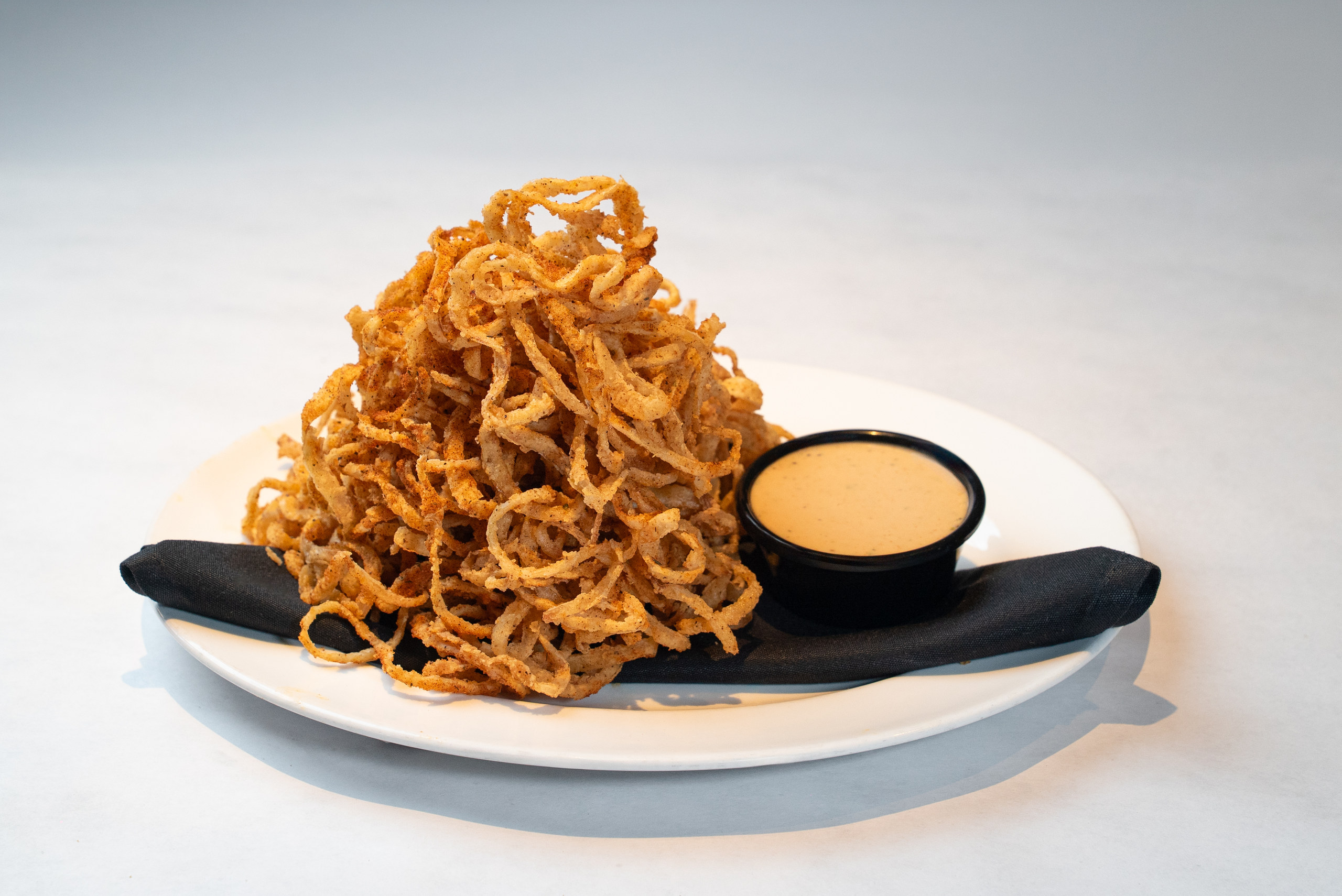 Tower of crispy seasoned onion strings with dipping sauce — Denver restaurant food photography